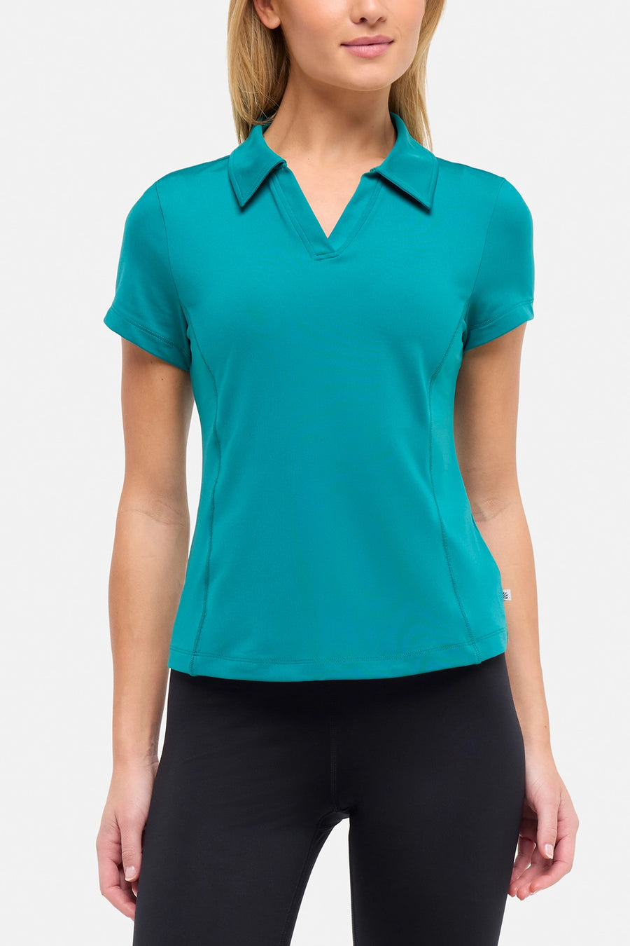 Front view of woman wearing a teal polo shirt and black pants on a white background. #color_quetzal-green