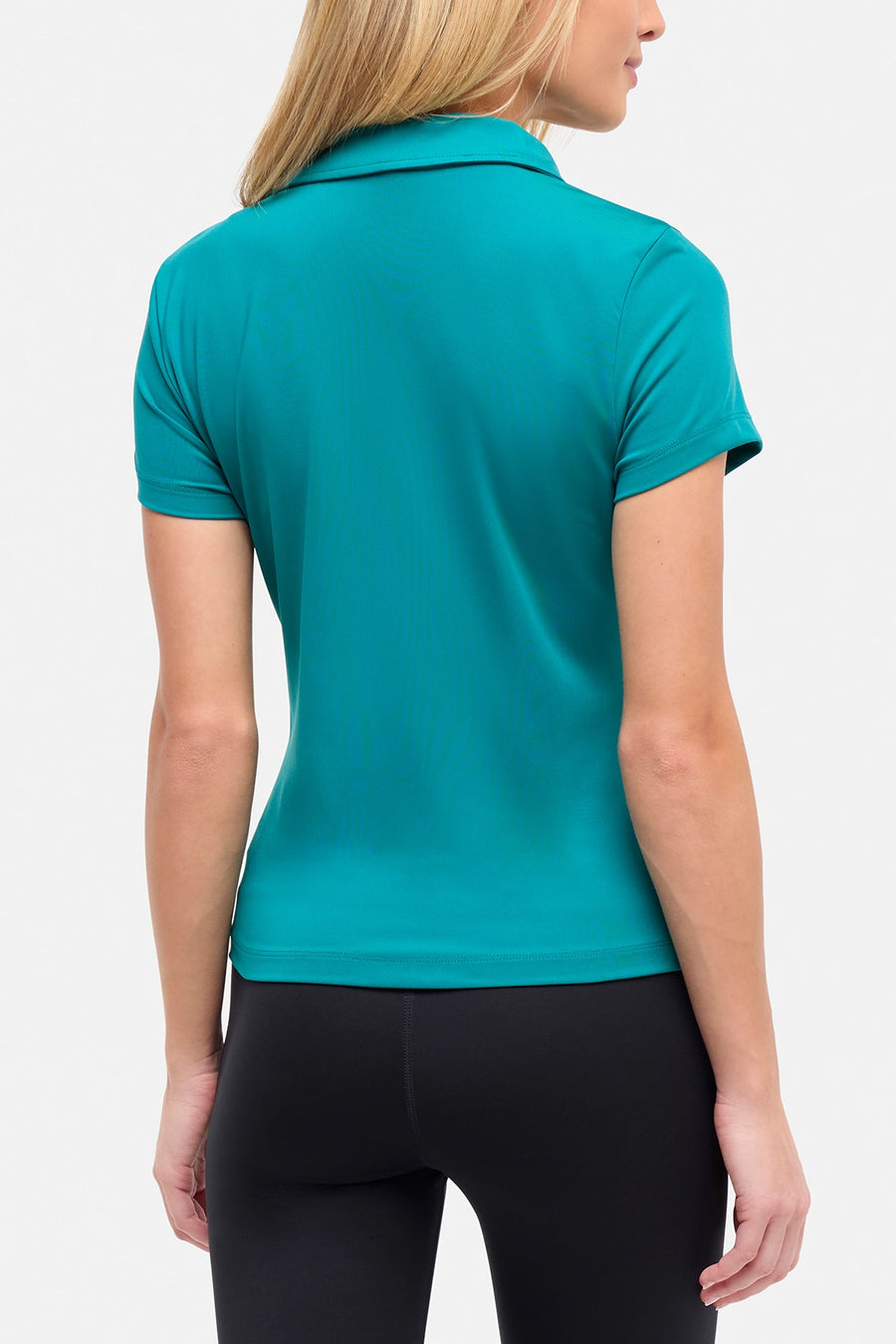 Back view of woman wearing a teal polo shirt and black pants on a white background. #color_quetzal-green