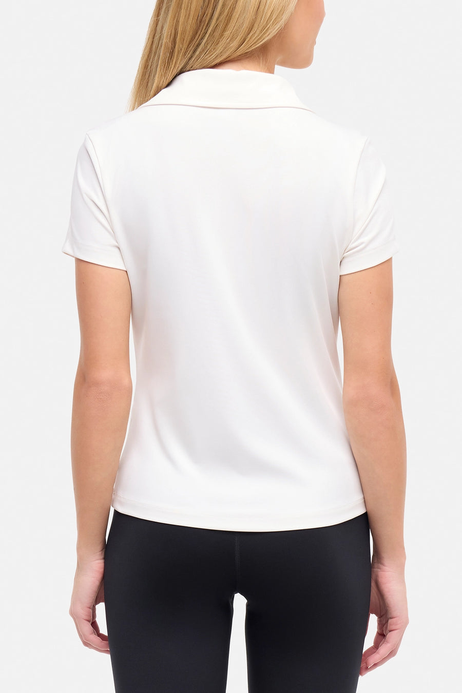 Back view of woman wearing a white short-sleeve polo shirt and black pants on a plain background. #color_sugar-swizzle