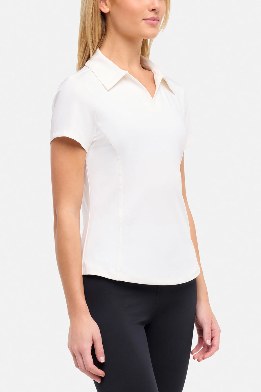 Side view of woman wearing a white short-sleeve polo shirt and black pants on a plain background. #color_sugar-swizzle