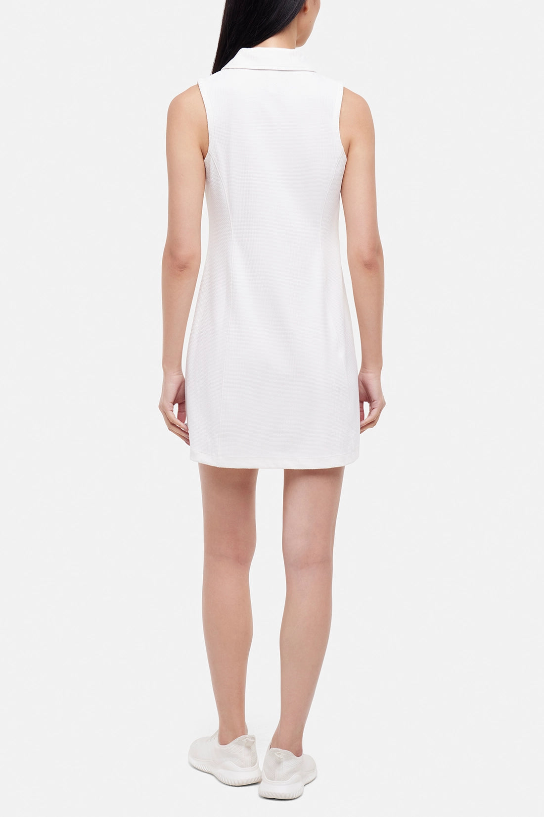 Back view of woman wearing a white sleeveless polo dress with a black stripe collar on a white background. 