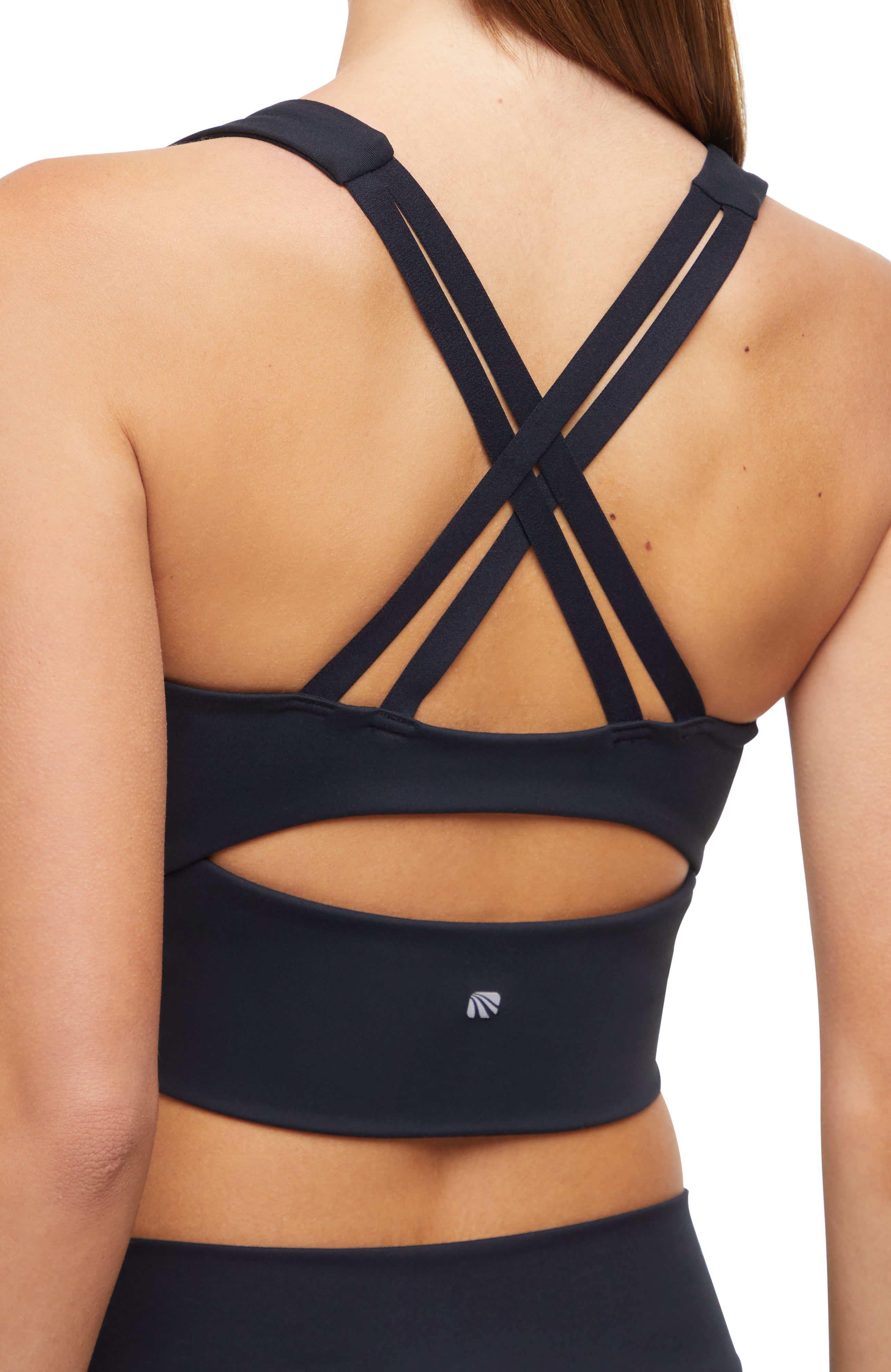 Close-up back view of woman wearing a black sports bra with criss-cross back design and black leggings on a white background. 