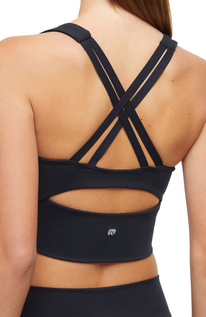 Close-up back view of woman wearing a black sports bra with criss-cross back design and black leggings on a white background. 