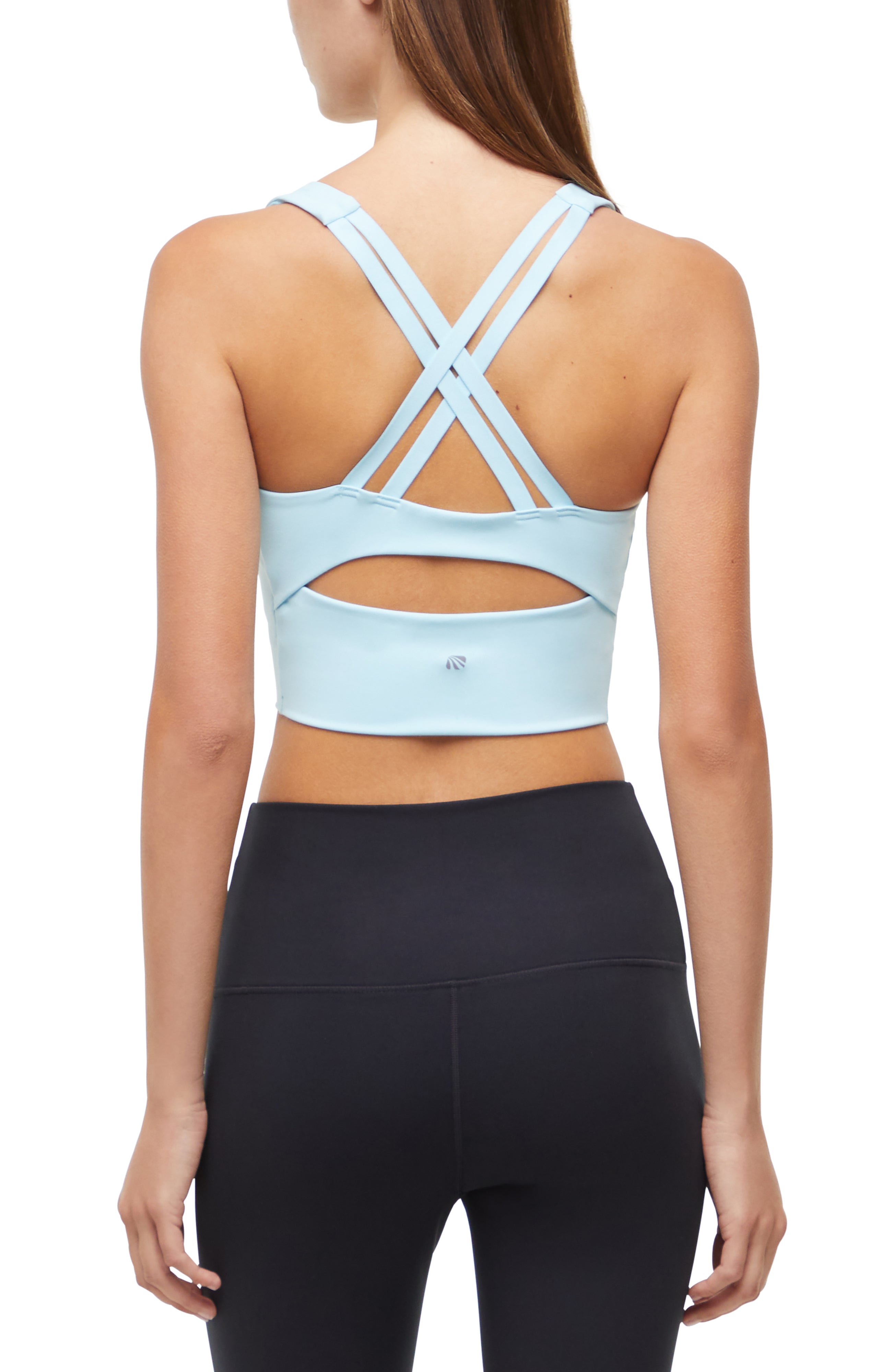 Back view of woman wearing a light blue sports bra with criss-cross back design and black leggings on a white background. 