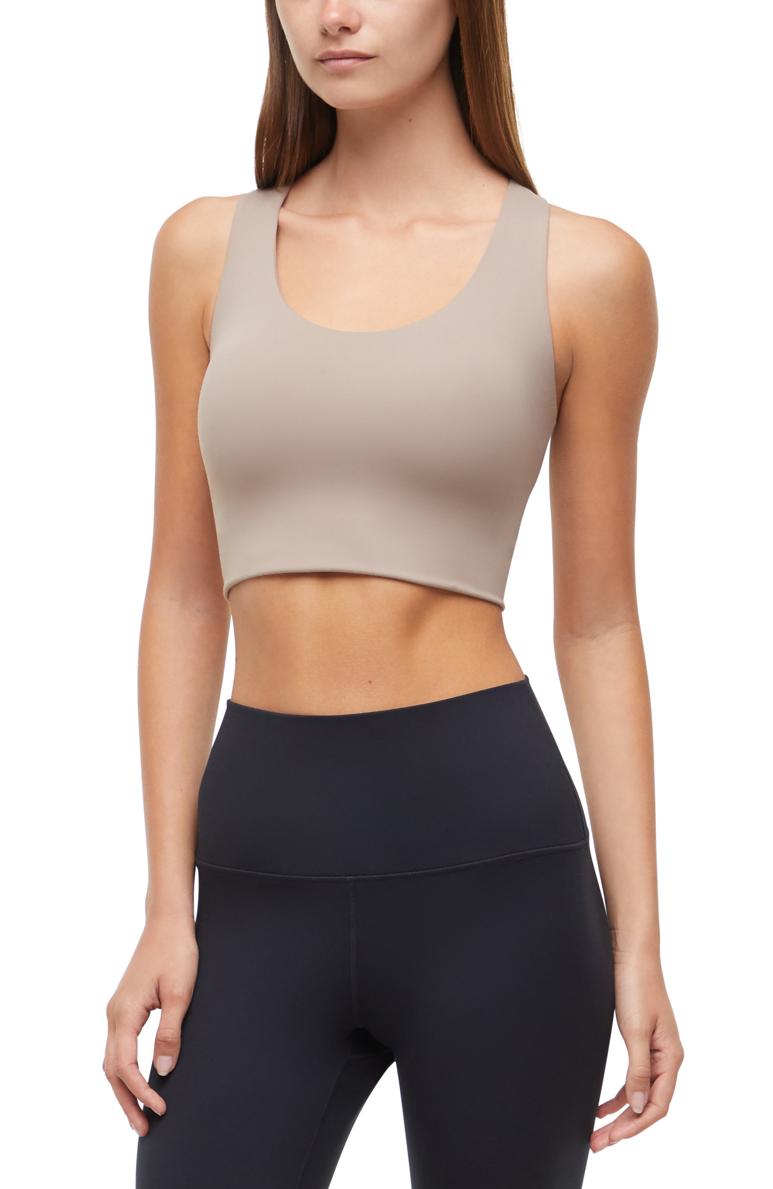 Front view of woman wearing a beige sports bra and black leggings on a white background. 