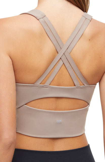Close-up back view of woman wearing a beige sports bra with criss-cross back design and black leggings on a white background. 
