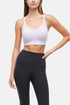Front view of woman wearing a lilac sports bra and black leggings on a light gray background. 