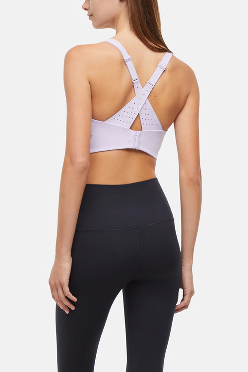 Back view of woman wearing a light purple sports bra with criss-cross straps and black leggings on a white background. #color_lilac-clematis