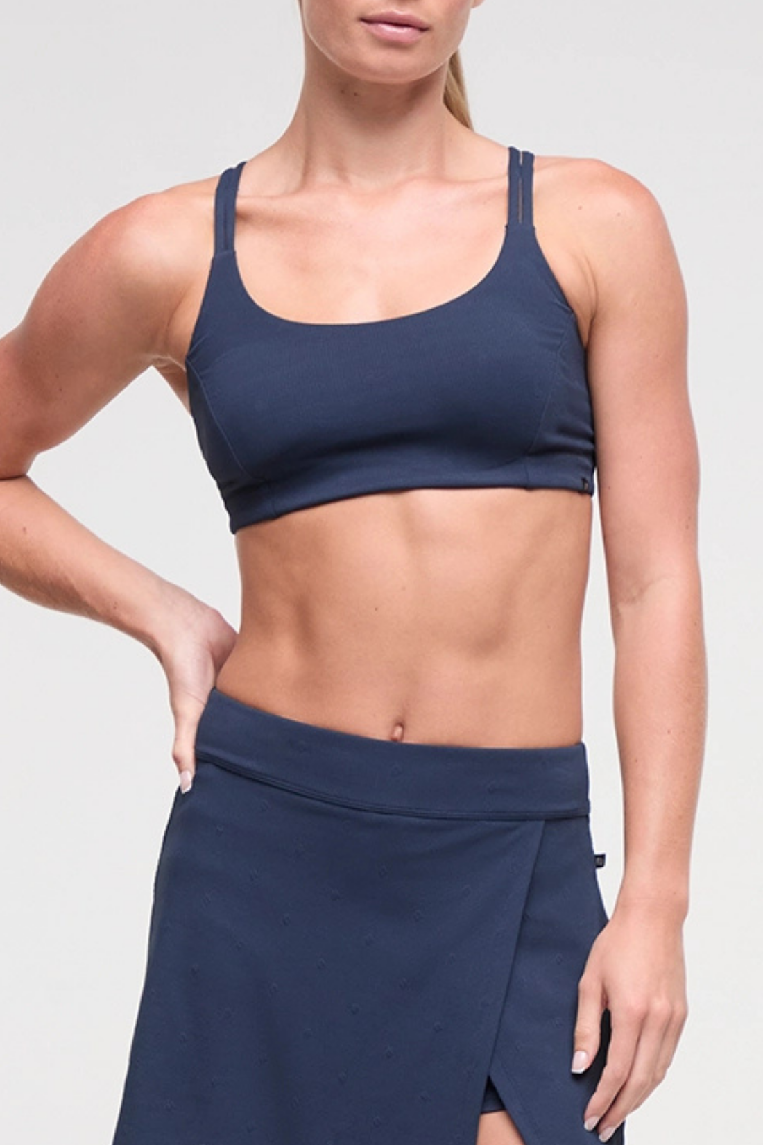 Front view of woman wearing a navy blue sports bra and skirt on a light gray background. 