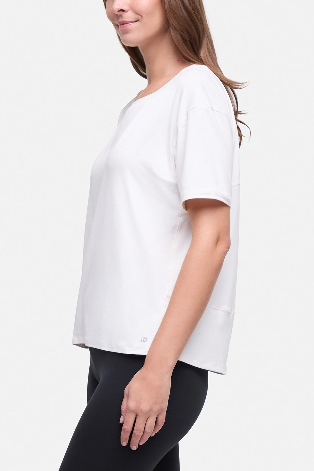 A woman wearing a white short-sleeve crewneck top and black leggings, shown from a side profile against a light gray studio background.  #color_sugar-swizzle