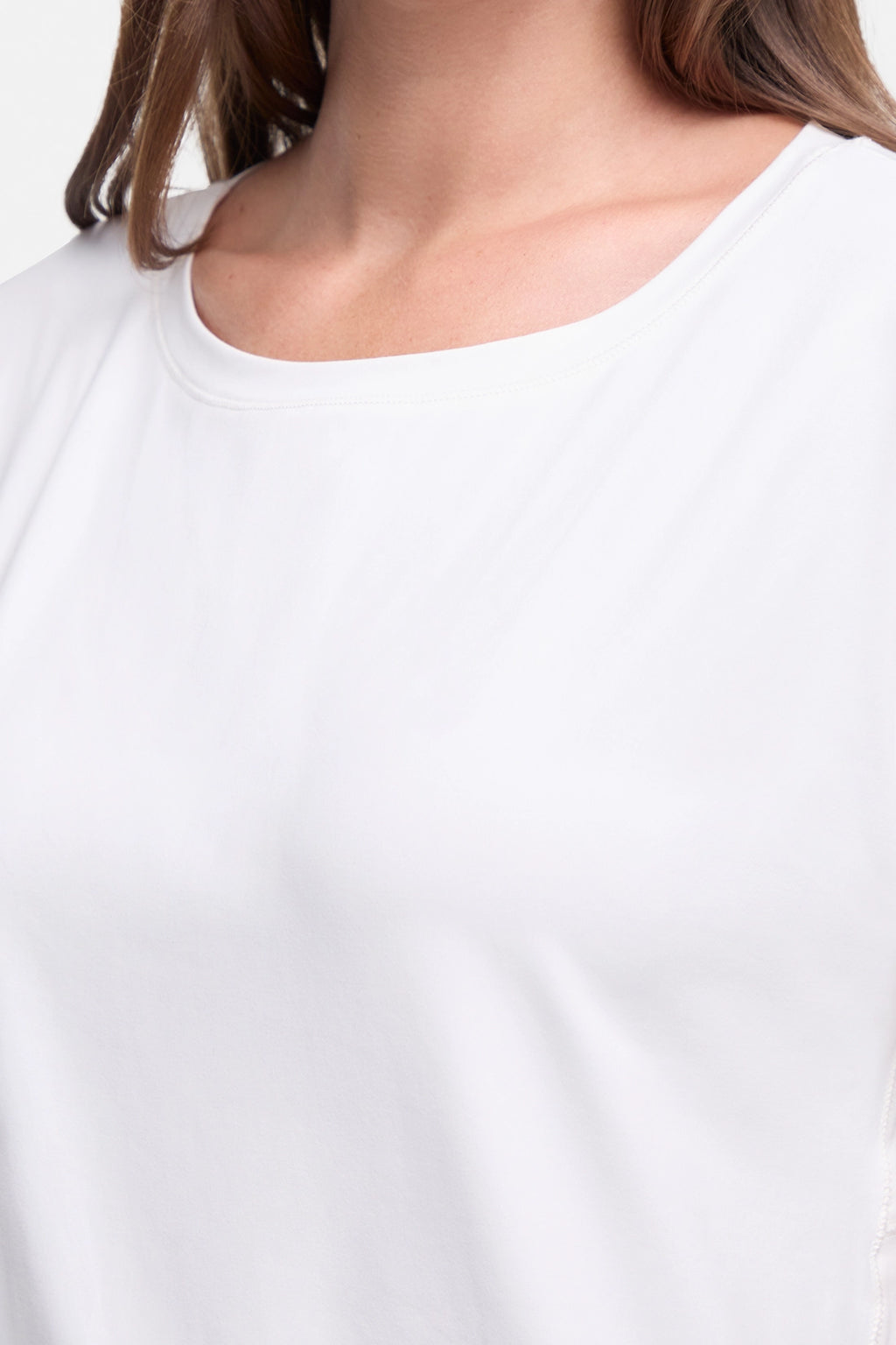 Close-up of a person wearing a plain white scoop-neck top, showing the neckline, skin, and a bit of brown hair against a light neutral background. #color_sugar-swizzle