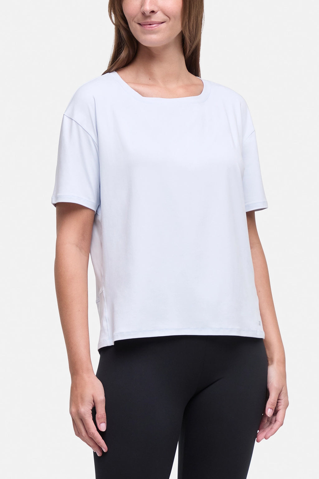 A woman wearing a light sky blue short-sleeve scoop-neck athletic top and black leggings, shown from the nose down against a light gray studio background. #color_ancient-water