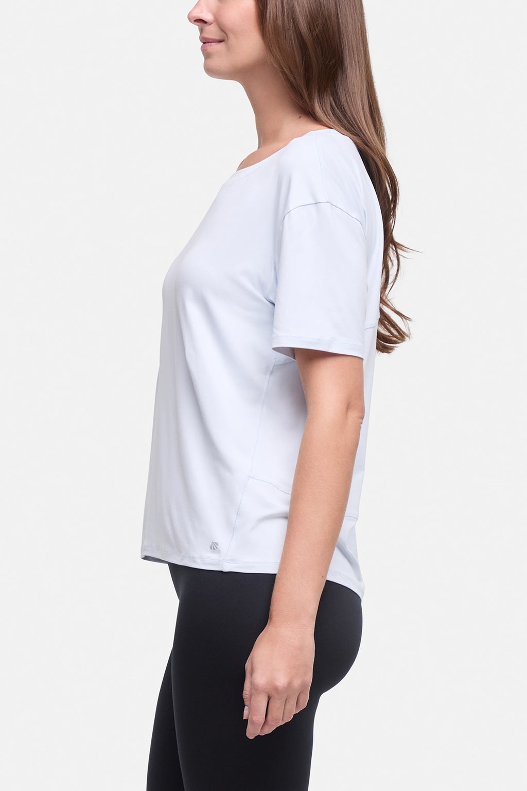A woman shown in side profile wearing a light blue short-sleeve athletic top and black leggings against a plain light gray studio background. #color_ancient-water