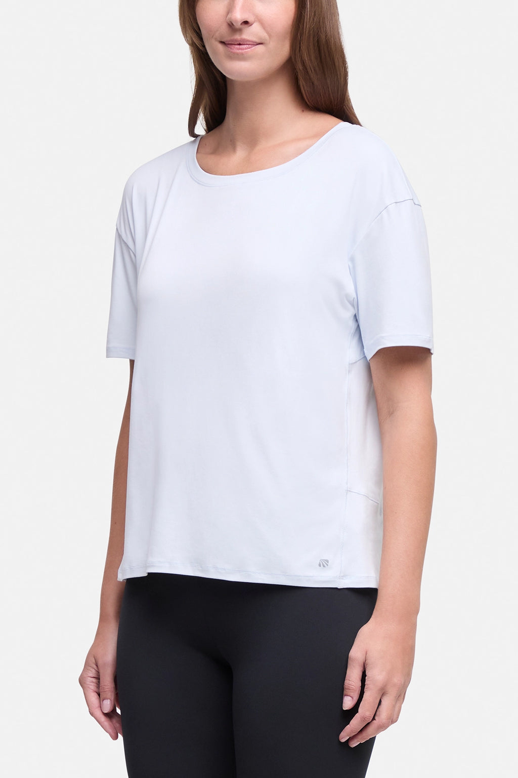 A woman wearing a light blue short-sleeve athletic top and black leggings, shown from the nose down against a plain light gray studio background. #color_ancient-water