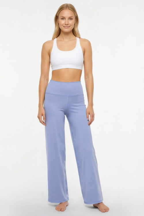 A woman modeling a two-piece activewear set consisting of a white sports bra and light periwinkle blue high-waisted wide-leg yoga pants, standing against a plain white studio background. #color_troposphere