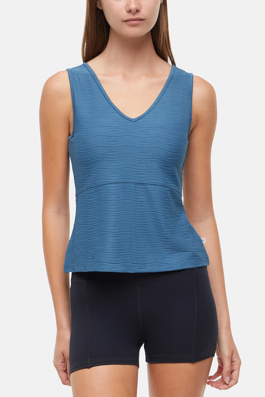 Woman wearing a blue v-neck  tank top and black shorts on a white background. 