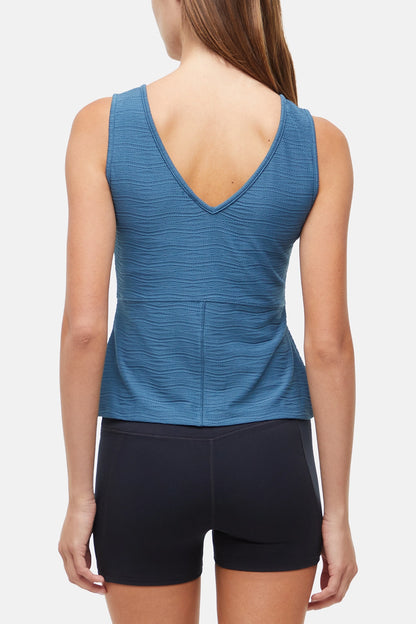 Back of Woman wearing a blue v-neck  tank top and black shorts on a white Background. 