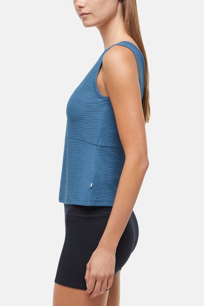 Side view of woman wearing a blue v-neck tank top and black shorts on a white background 