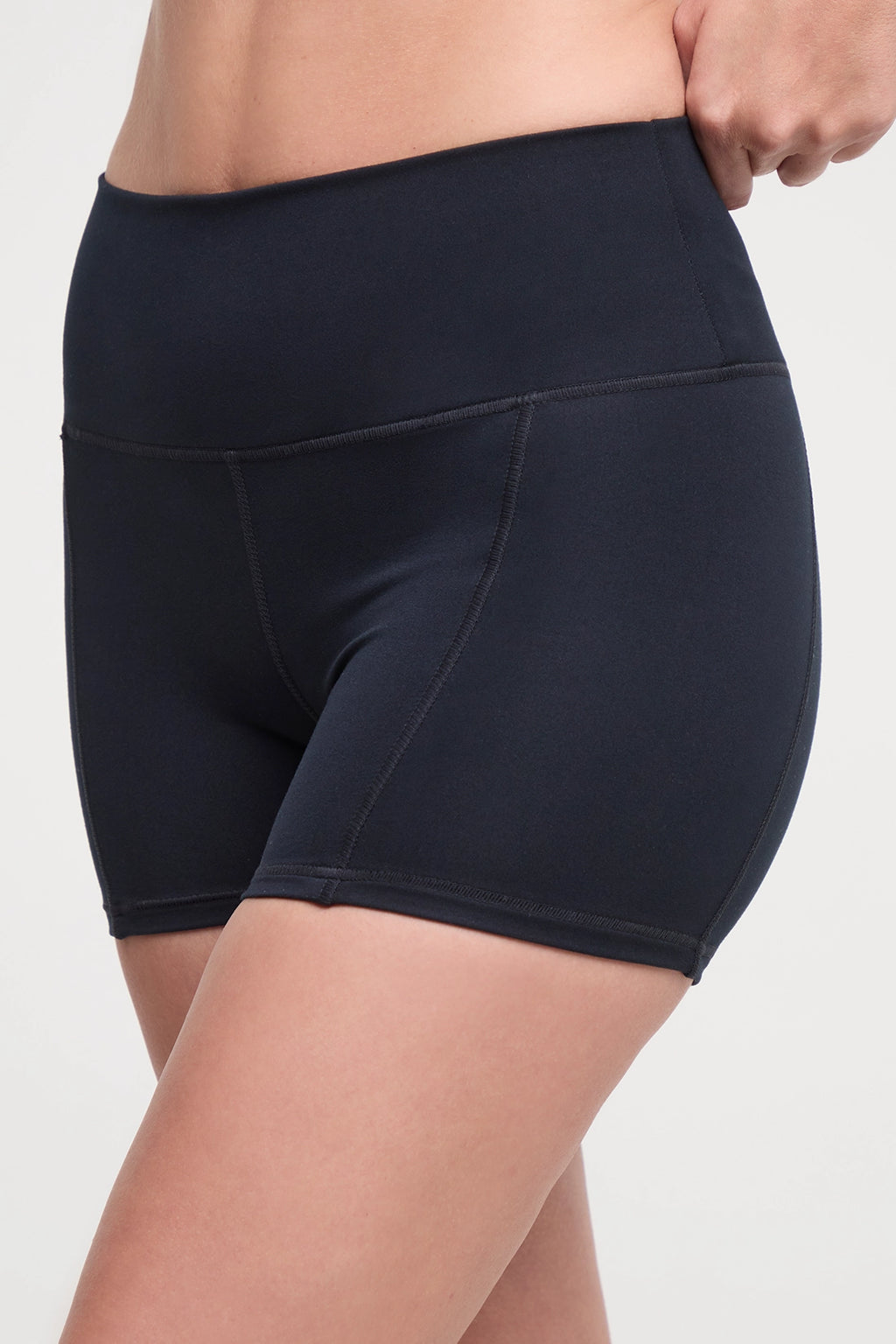 Close up front view of woman wearing black athletic shorts and white sneakers on a light background. #color_black