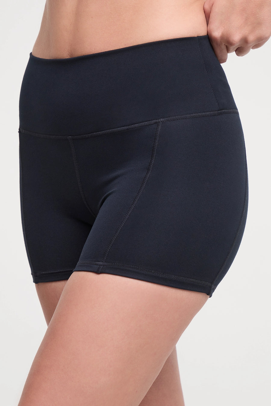 Close up front view of woman wearing black athletic shorts and white sneakers on a light background. #color_black