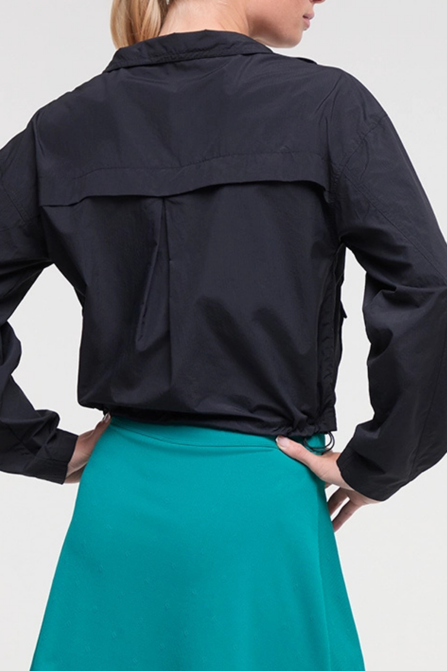 Back view of woman wearing a black jacket and teal skirt on a white background. #color_black