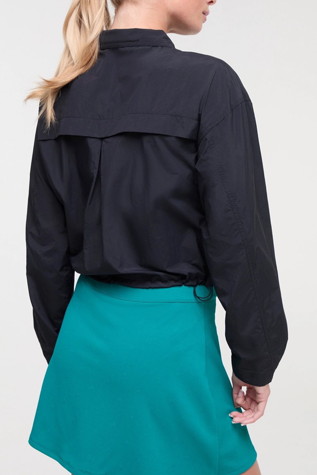 Back view of woman wearing a black jacket and teal skirt on a white background. 