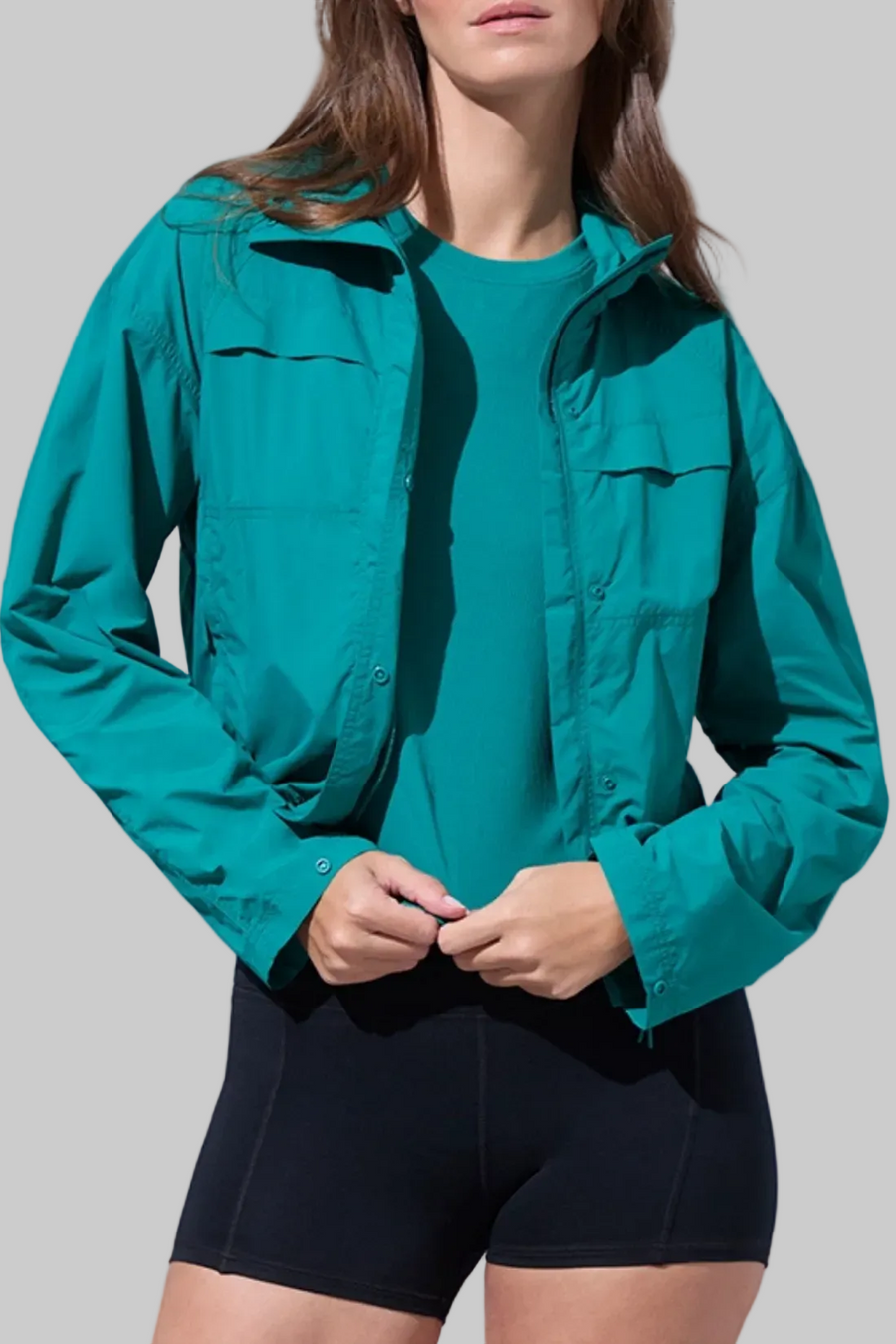 Front view of woman wearing a teal jacket and black shorts on a white background. #color_quetzal-green