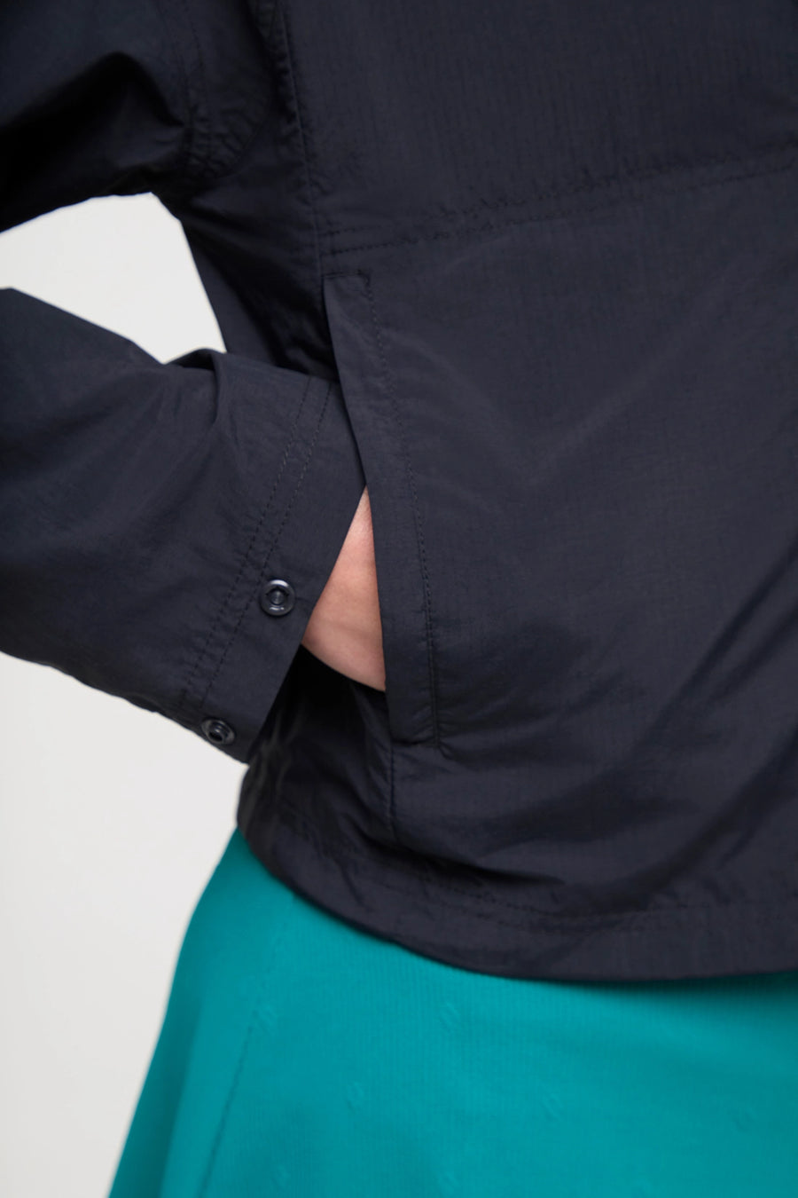 Close up zipper pocket detail view of woman wearing a black jacket and teal skirt on a white background. #color_black