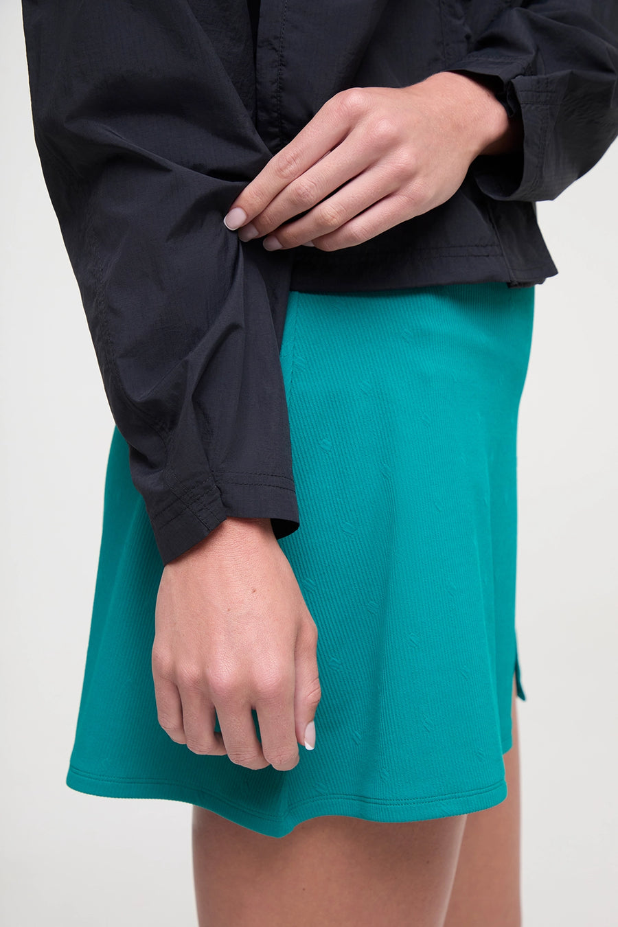 Close up sleeve detail view of woman wearing a black jacket and teal skirt on a white background. #color_black