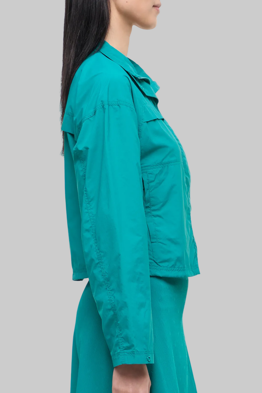 Side view of woman wearing a teal jacket and skirt on a white background. #color_quetzal-green