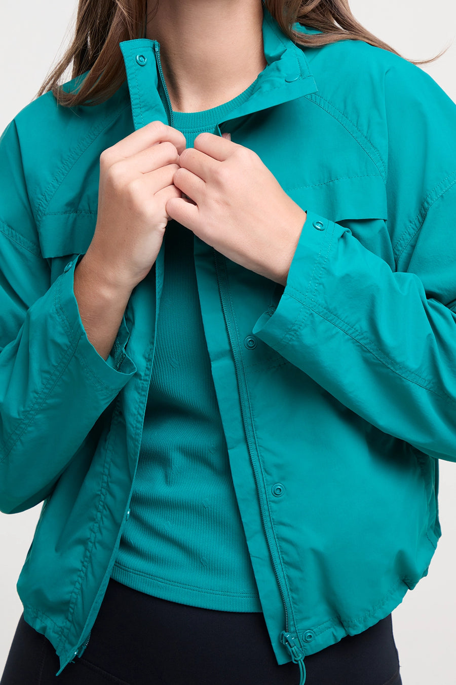 Front view of woman wearing a teal jacket and black shorts on a white background. #color_quetzal-green