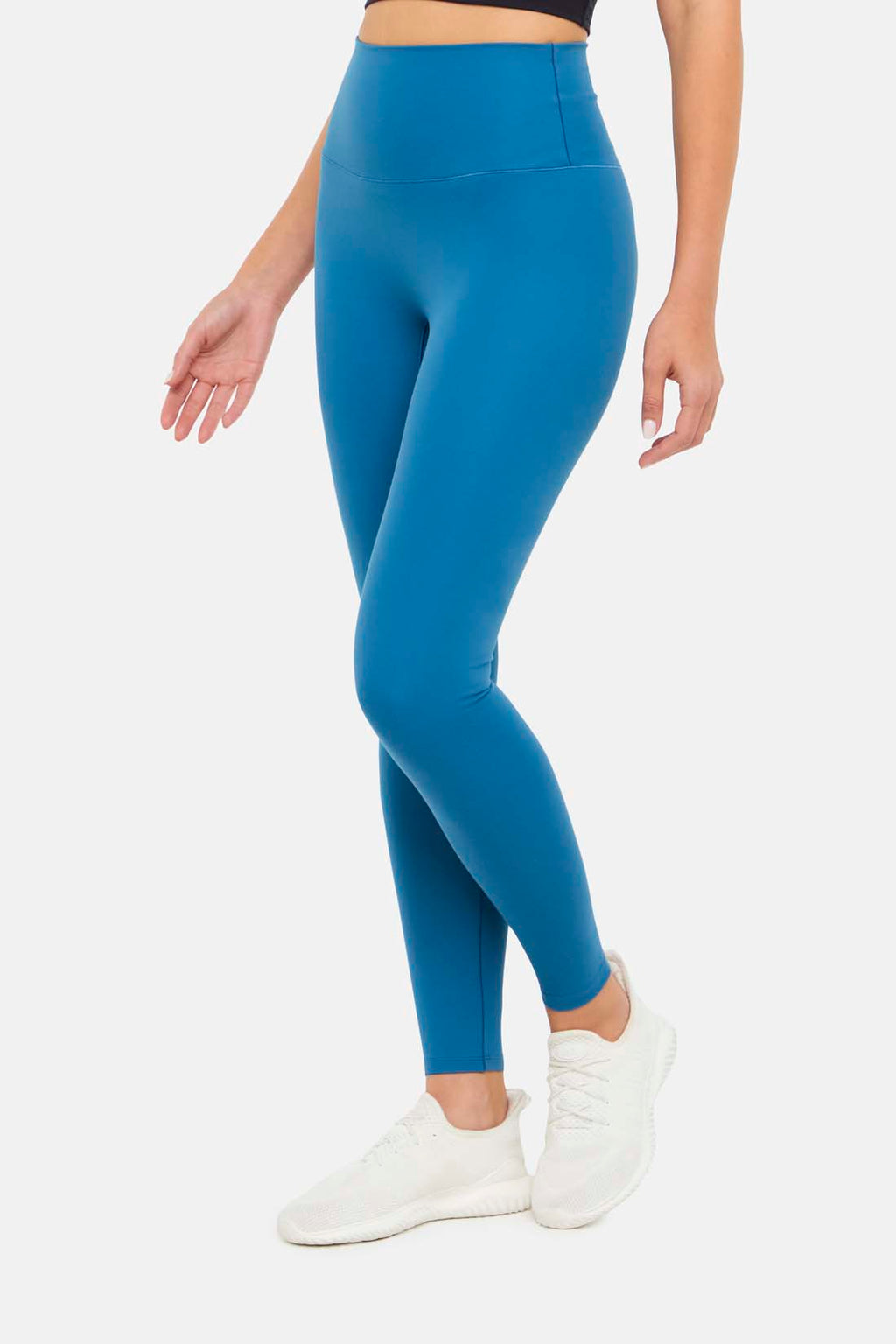 Side view of woman wearing bright blue leggings on a white background. #color_midnight