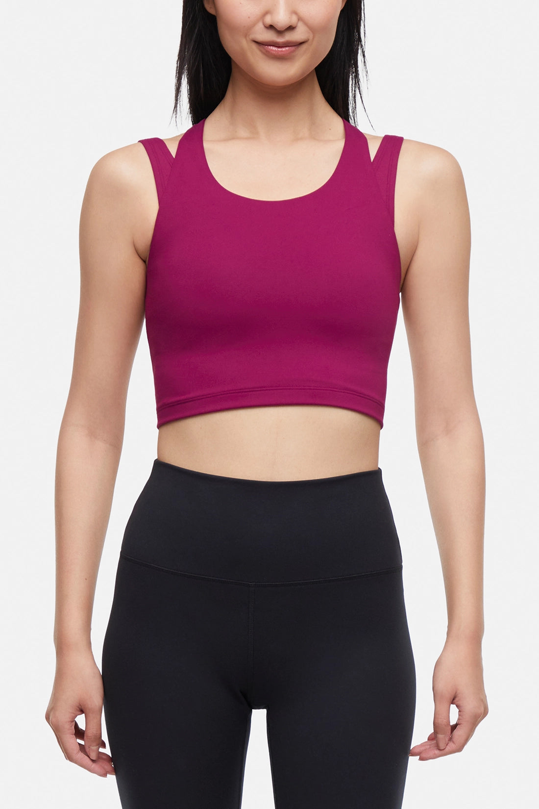 Front view of woman wearing a bright burgundy sports bra and black leggings on a white background. 