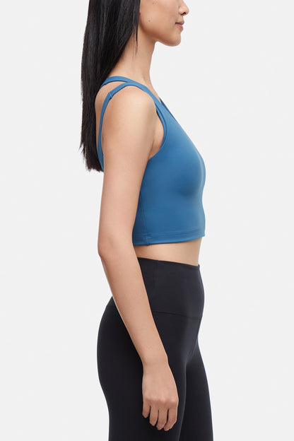 Side view of woman wearing a blue sports bra and black leggings on a white background. 