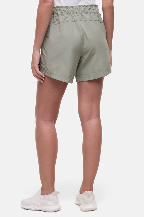 Back view of woman wearing sage green shorts and white sneakers on a white background. #color_shadow