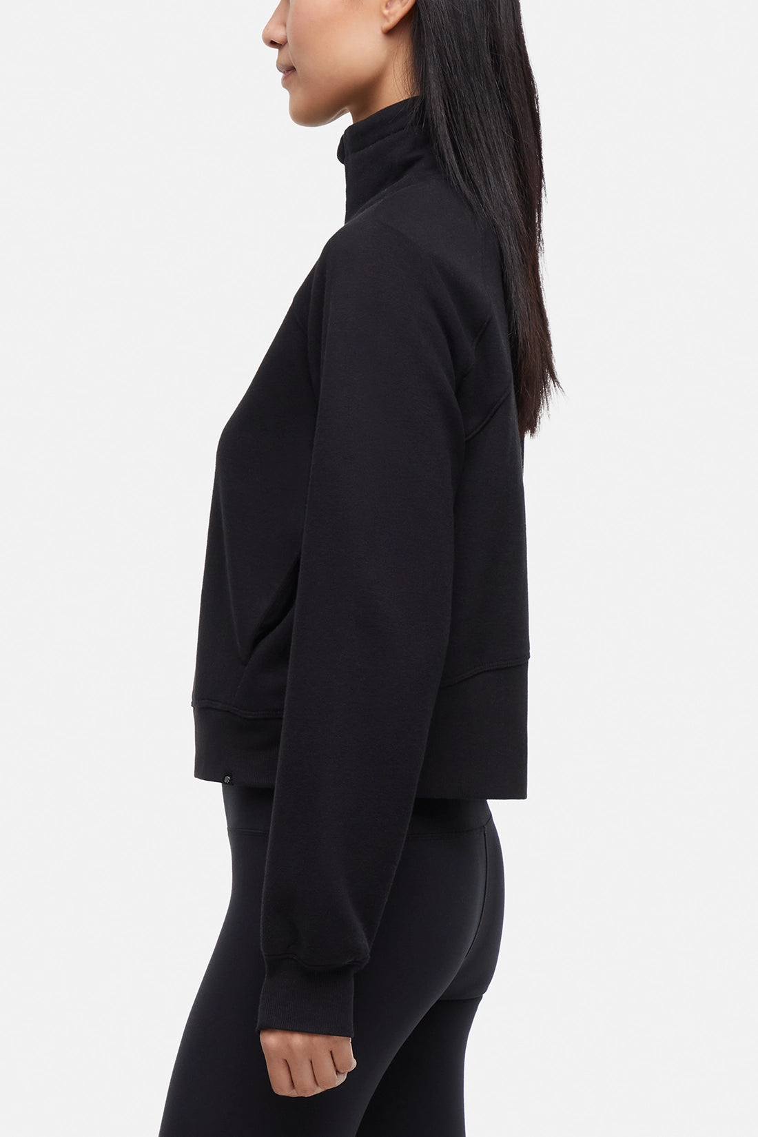 Side view of woman wearing black half-zip pullover with thumbholes on a white background.