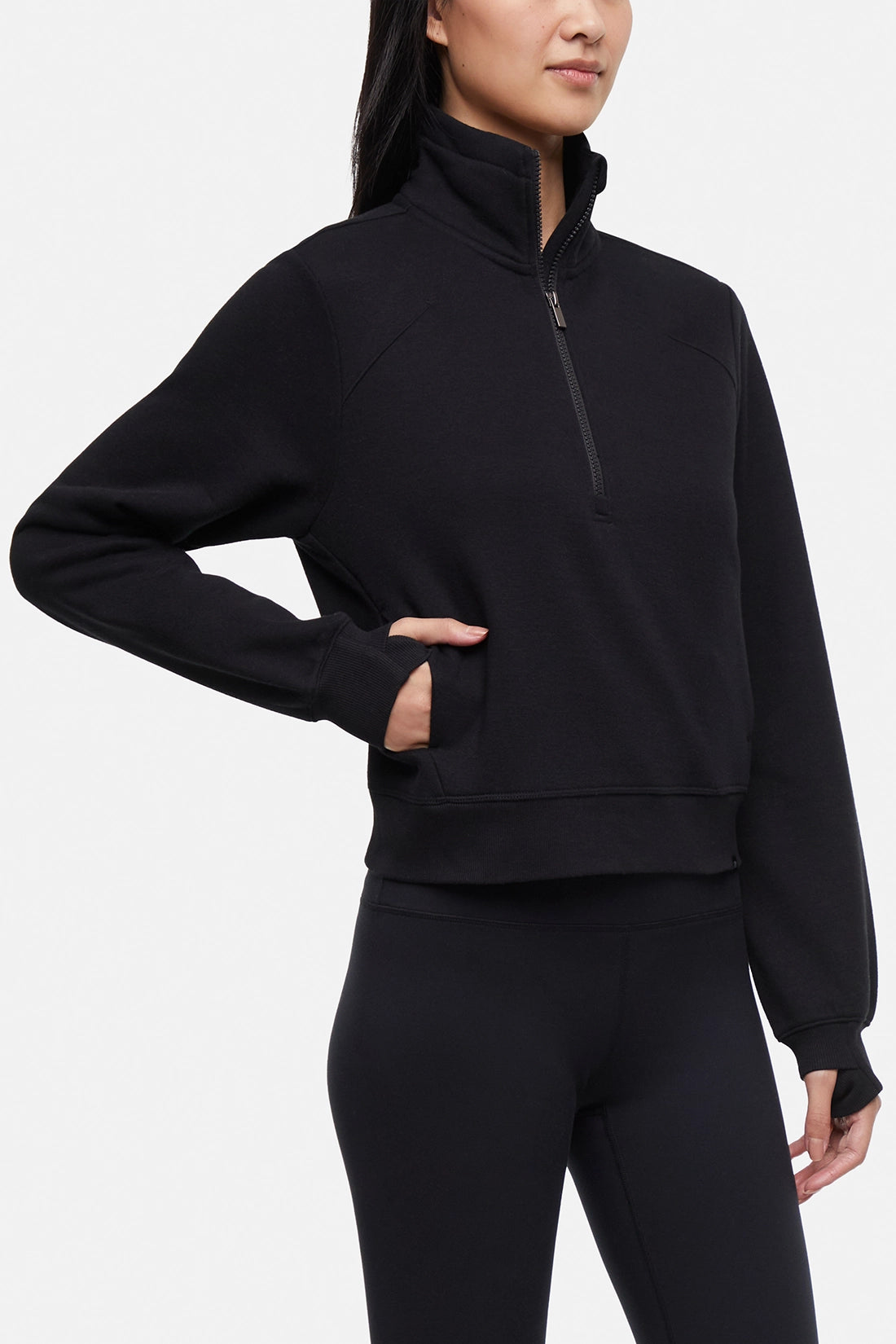 Front view of woman wearing black half-zip pullover with thumbholes on a white background.