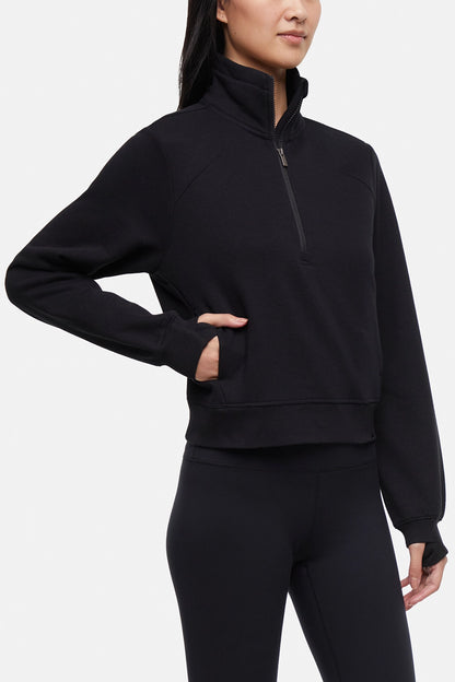 Front view of woman wearing black half-zip pullover with thumbholes on a white background. 