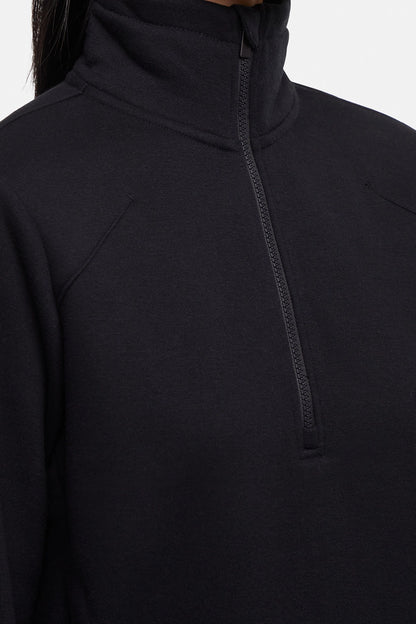 Front close up view of woman wearing black half-zip pullover with thumbholes on a white background. 