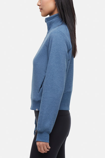 Side view of woman wearing heather blue half-zip pullover with thumbholes on a white background. 