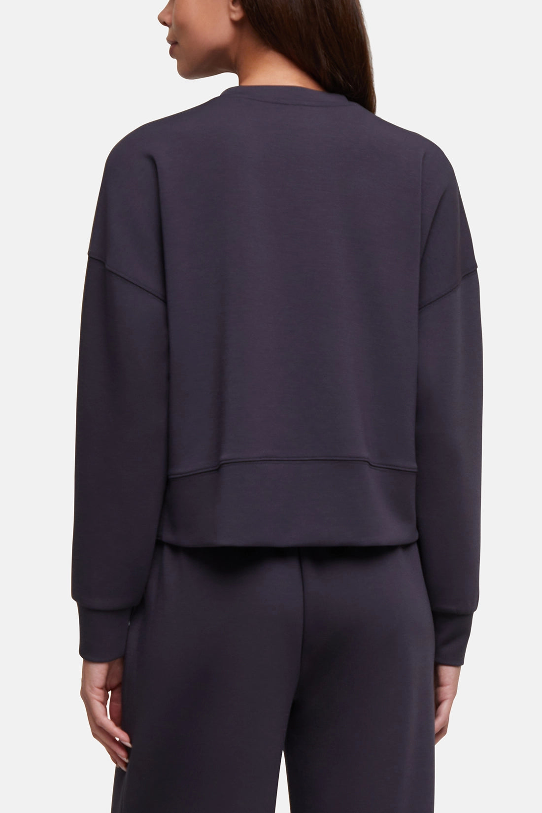 A woman shown from the back wearing a dark charcoal gray cropped sweatshirt and matching sweatpants against a light gray studio background. 