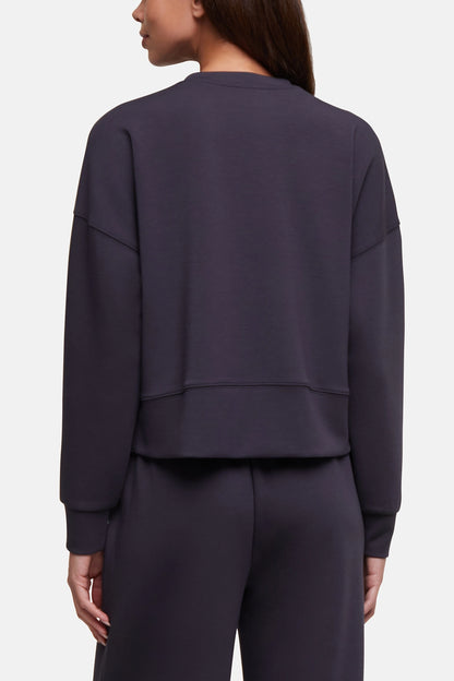 A woman shown from the back wearing a dark charcoal gray cropped sweatshirt and matching sweatpants against a light gray studio background. 