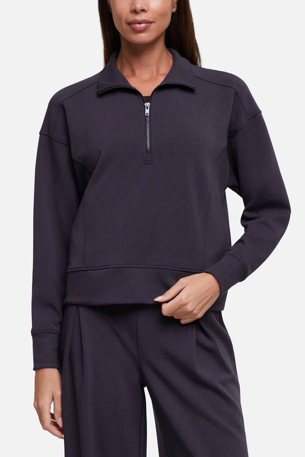 A woman wearing a dark navy long-sleeve quarter-zip sweatshirt and matching sweatpants against a light gray studio background.