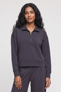 A woman modeling a dark charcoal gray half-zip sweatshirt and matching sweatpants against a light gray studio background.