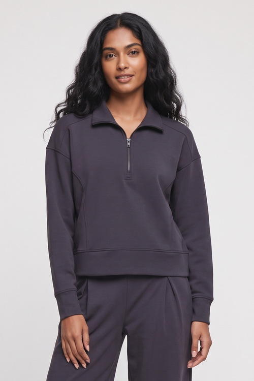 A woman modeling a dark charcoal gray half-zip sweatshirt and matching sweatpants against a light gray studio background.