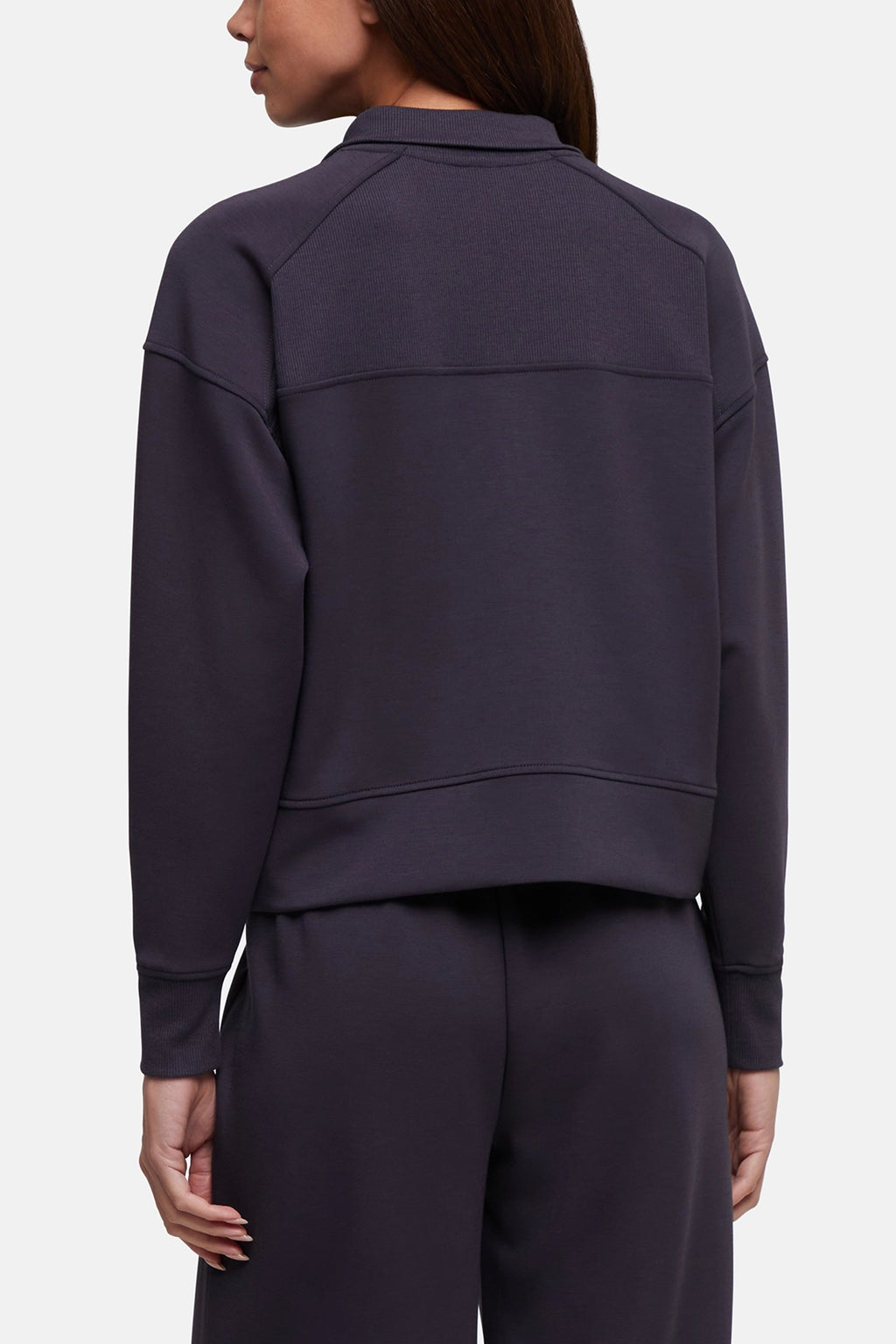 Rear view of a model wearing a dark charcoal gray cropped sweatshirt and matching sweatpants against a light gray studio background.