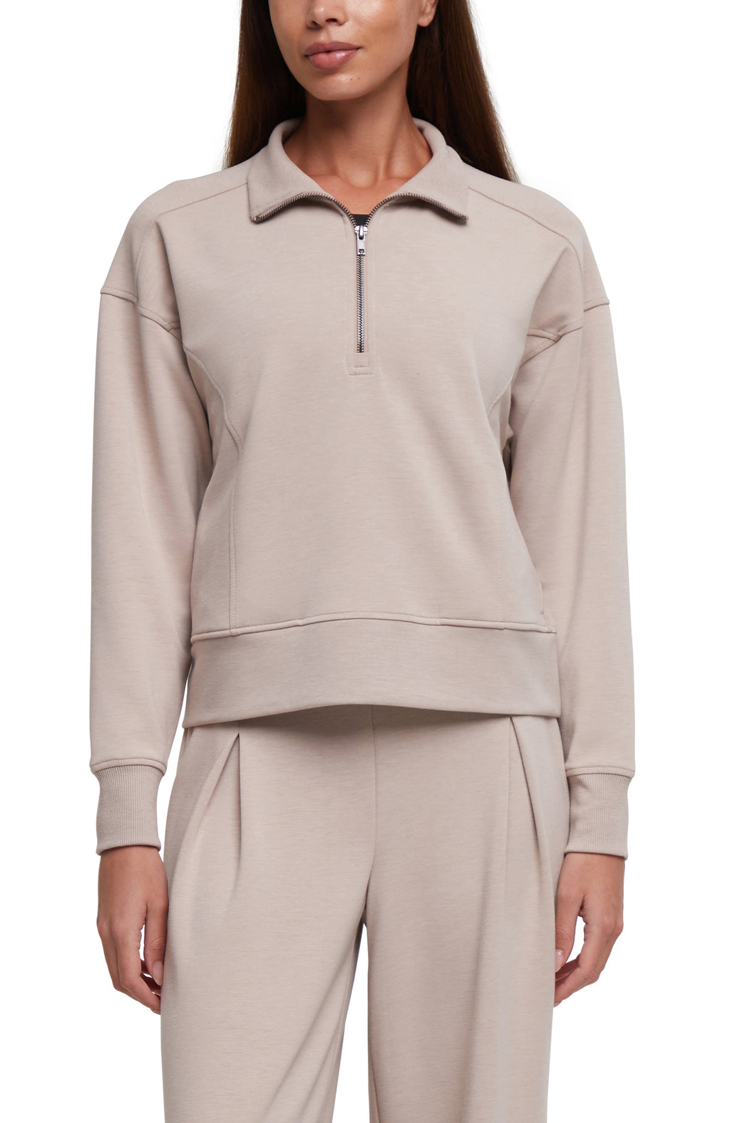 A woman wearing a light beige half-zip sweatshirt and matching sweatpants against a plain white background.