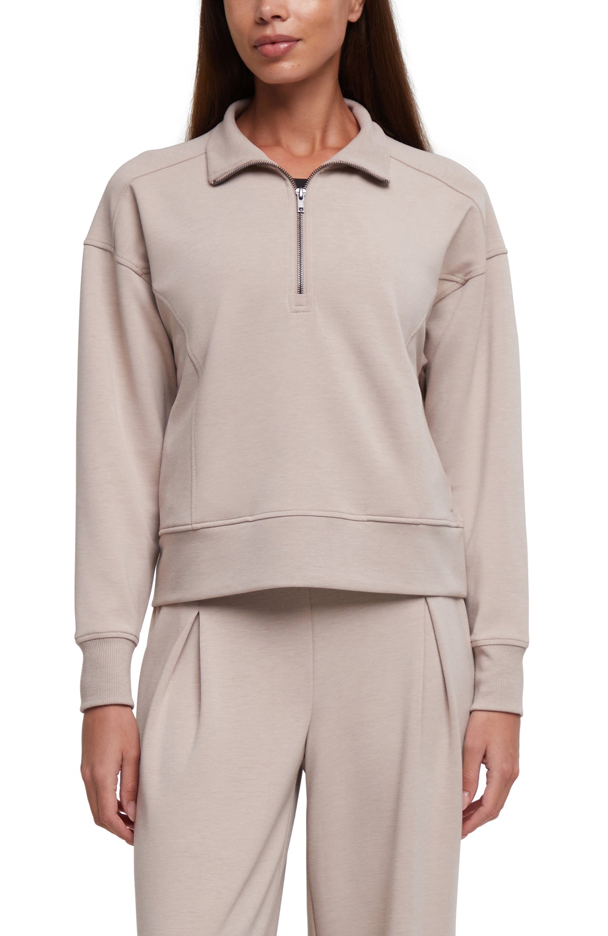 A woman wearing a light beige half-zip sweatshirt and matching sweatpants against a plain white background.