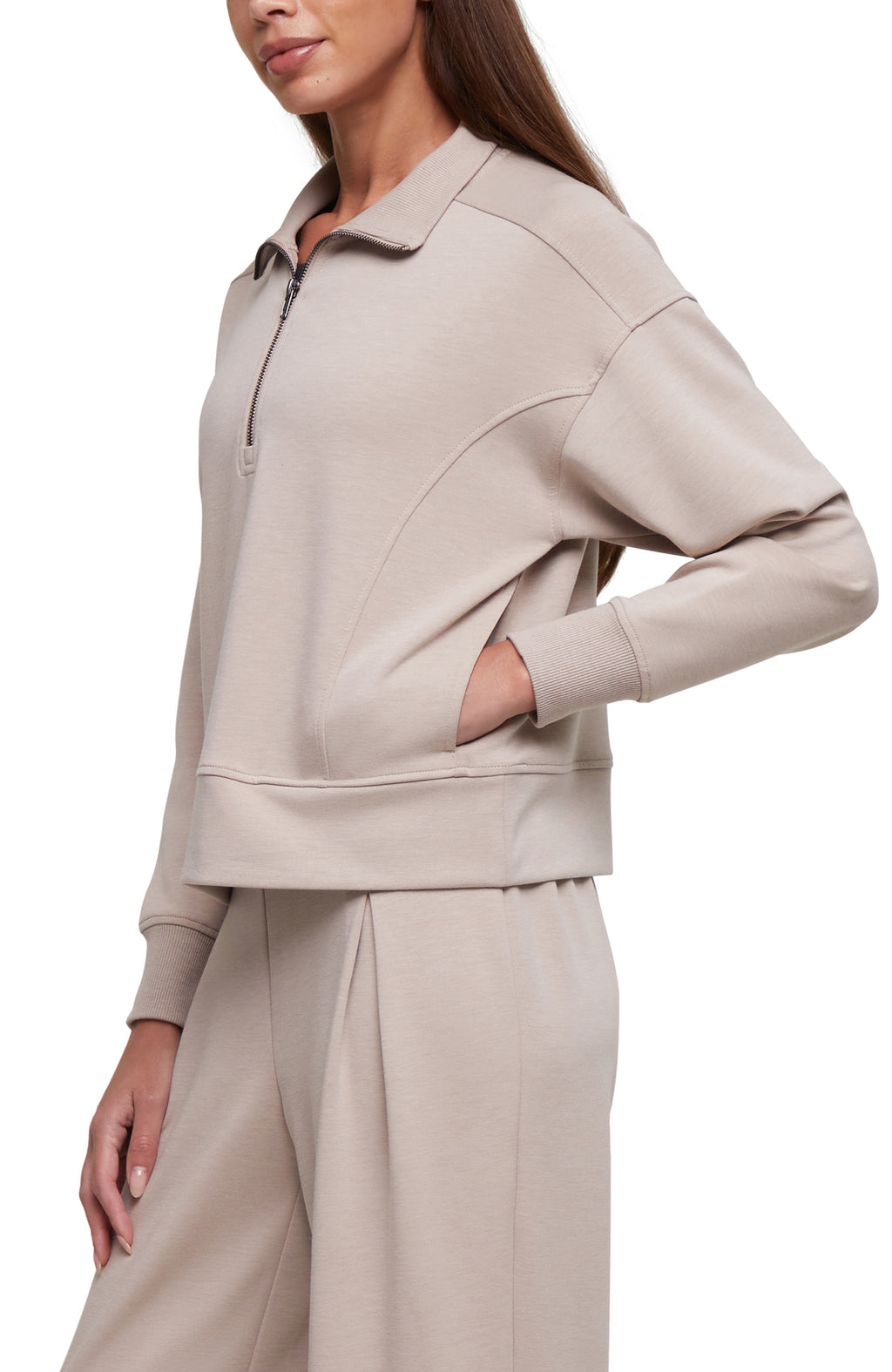 A woman wearing a light beige half-zip pullover sweatshirt with matching wide-leg sweatpants, shown from the side against a plain white background.