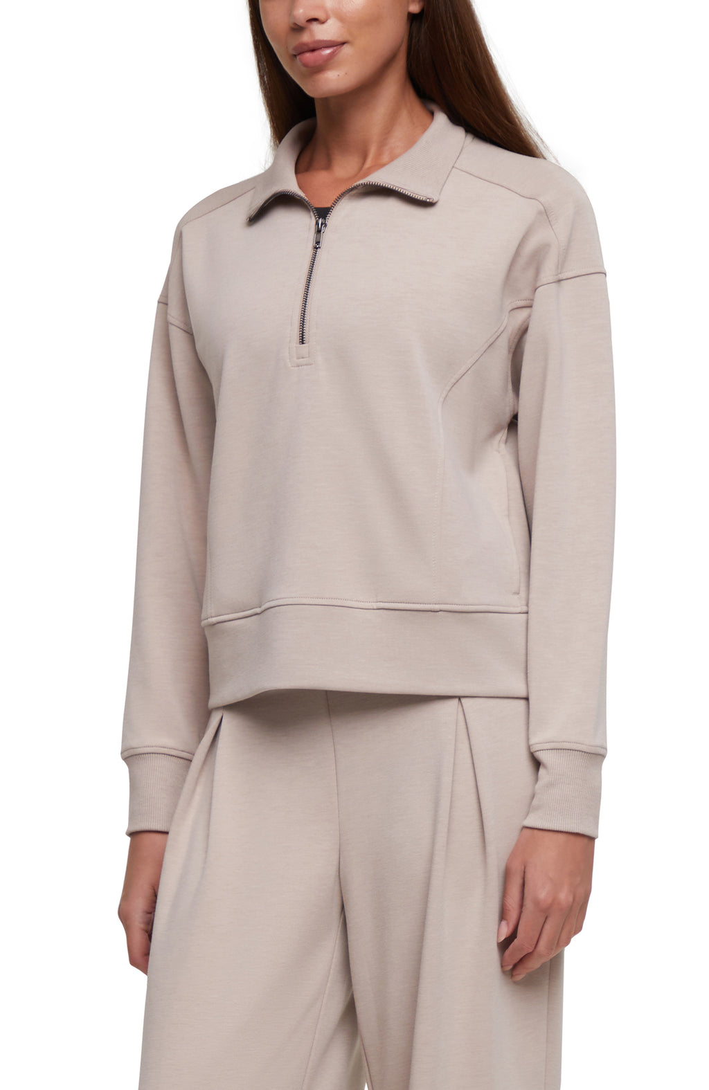 A woman wearing a light beige half-zip pullover sweatshirt with matching wide-leg sweatpants, shown from the neck down against a plain white background.